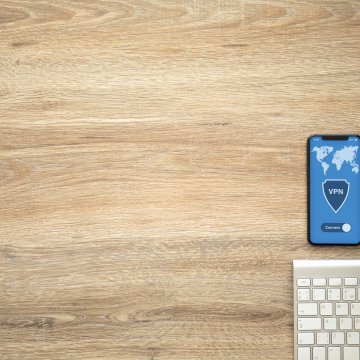 surfshark vpn services price cost smartphone connected to vpn white latop keyboard on wooden desk